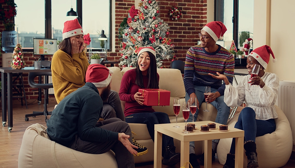 colleghi con cappellini natalizi che si scambiano regali per la festa di natale aziendale